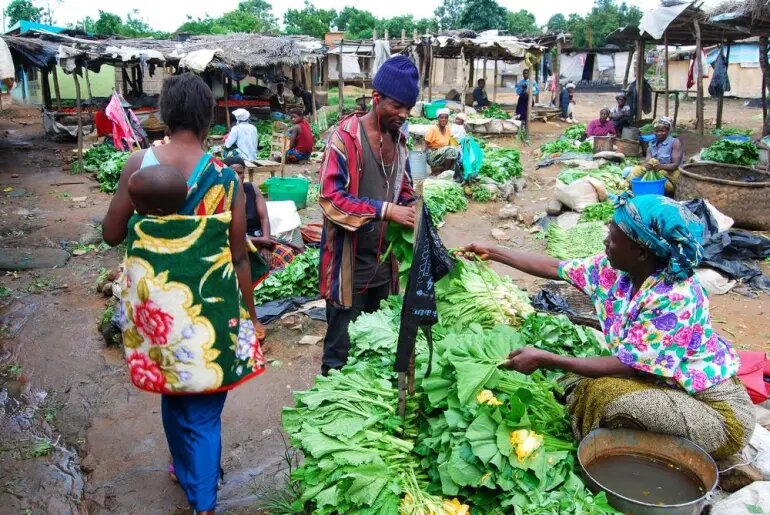 A market trader selling vegetables to a customer at an open-air market